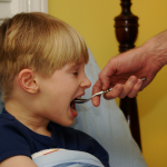 A young child being given medicine by an adult caregiver, representing safe and supervised medication use for children.
